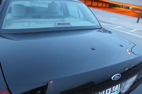 2007 Ford Crown Victoria - Close, low angle across the black decklid of a Ford sedan, with the Ford blue oval badge, two blanked-off holes where a spoiler or antenna…