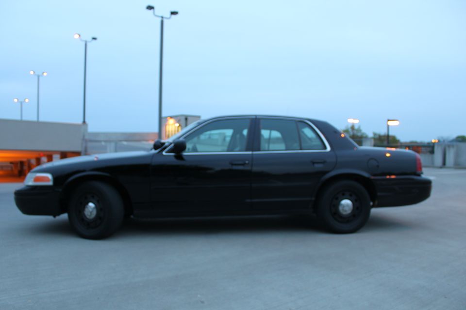 Side profile of a black full-size sedan on black steel wheels on a parking deck at dusk