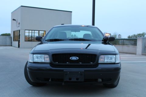 2007 Ford Crown Victoria - Head-on front view of a black Ford Crown Victoria with blacked-out honeycomb grille and Ford blue oval, amber pillar spotlight on the passe…