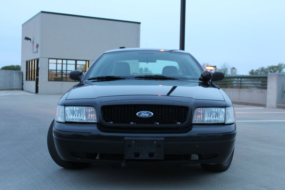 Black Ford Crown Victoria front view with black grille, Ford oval and amber A-pillar spotlight
