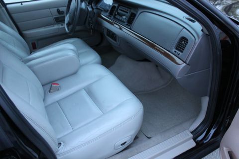 2007 Ford Crown Victoria - The interior of a car features light gray leather seats and a dashboard with wood-grain accents.