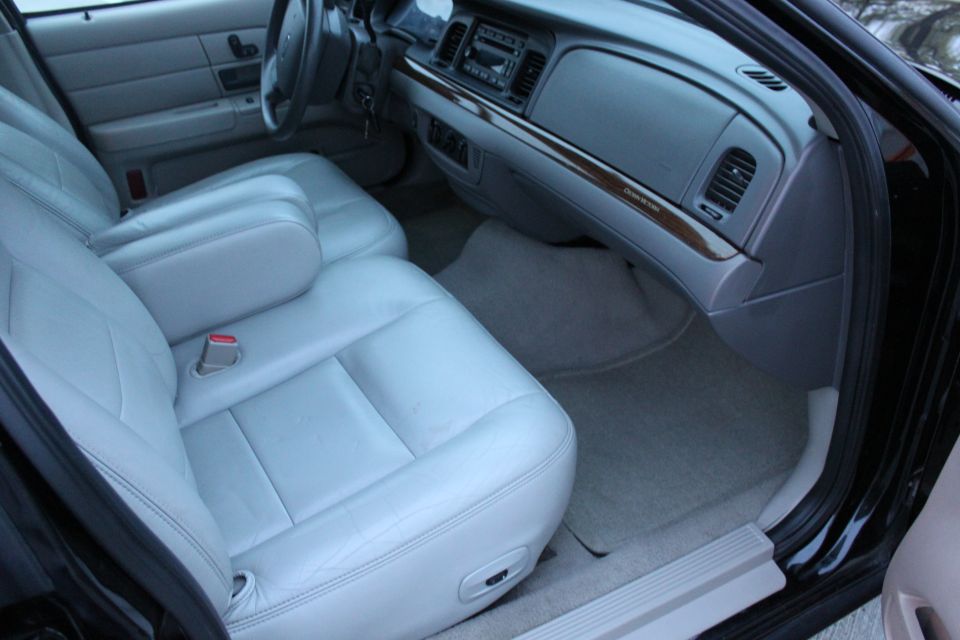 Interior of a car with light gray leather seats and a wood-grain trim dashboard. The steering wheel and center console are visible