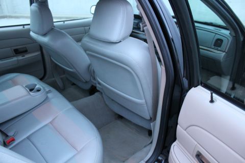 2007 Ford Crown Victoria - Rear passenger compartment of a sedan viewed through the open rear door, showing generous legroom, gray carpet and light gray leather front…