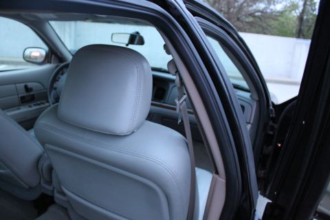 2007 Ford Crown Victoria - Interior view from the rear door of a black sedan, looking at the back of the light gray leather driver's seat and headrest with the B-pill…