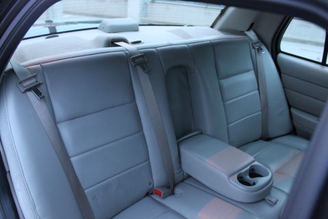 2007 Ford Crown Victoria - Rear cabin of a full-size sedan photographed from the open rear door, showing a light gray leather bench with the center armrest folded dow…