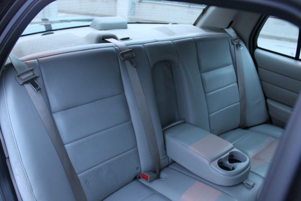 Light gray leather rear seat of a sedan with folded-down armrest, cup holders and shoulder belts