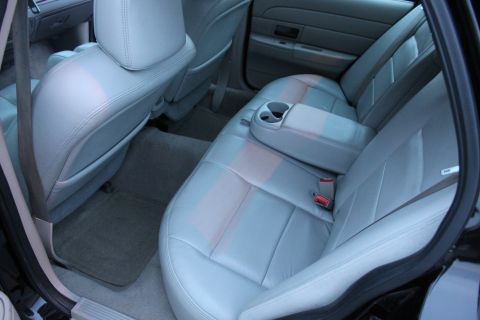 2007 Ford Crown Victoria - Rear bench seat of a full-size sedan shot through the open rear door, upholstered in light gray leather with a fold-down center armrest con…