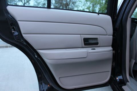 2007 Ford Crown Victoria - Inner panel of an open rear door on a black sedan, upholstered in light gray with a chrome-trimmed inside handle, a single power window swi…