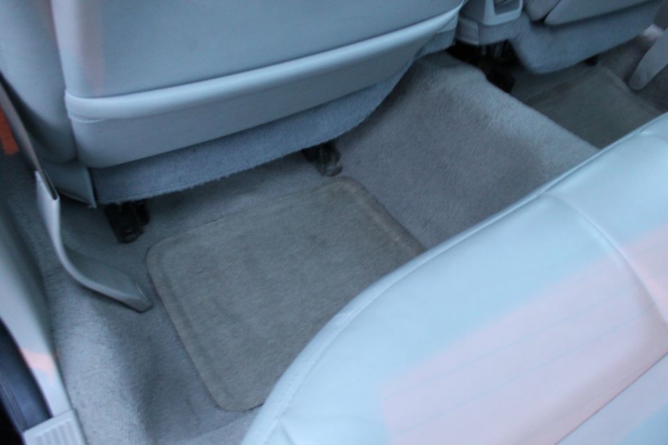 Gray rear passenger footwell of a sedan with carpeted floor mat and rear bench edge