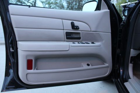 2007 Ford Crown Victoria - Inner panel of an open driver's door on a black sedan, trimmed in light gray with a power mirror joystick, chrome-trimmed door handle, spea…