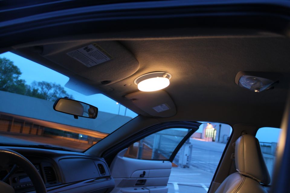 Sedan interior at dusk with illuminated dome light, tan headliner, visors and leather seats