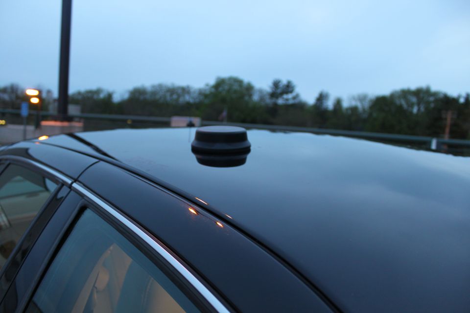 Black puck antenna mounted on the dark roof of a sedan, chrome window trim below