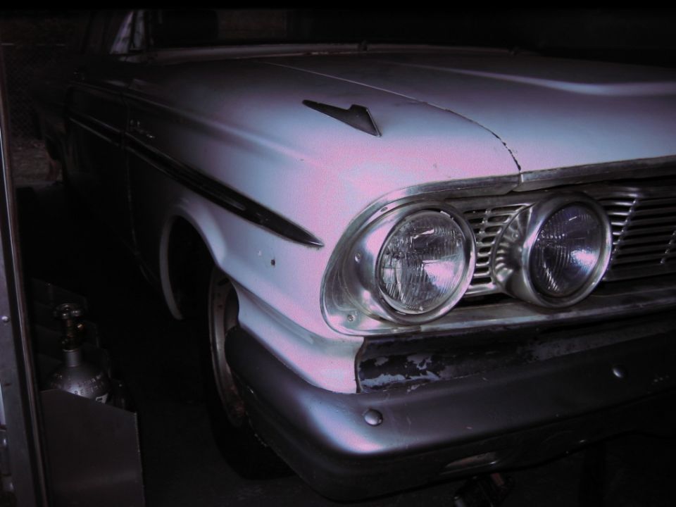 Front corner of a light-colored 1960s Ford Fairlane. Dual headlights and grille visible