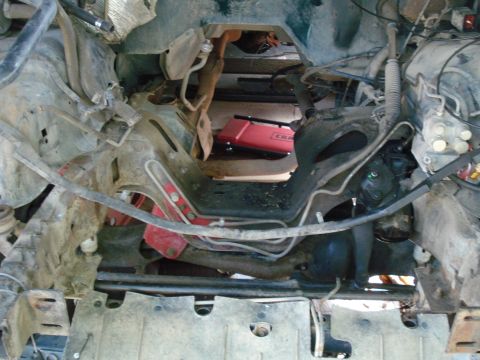 1993 Ford Bronco - The engine bay of a vehicle is shown with various mechanical parts and a red jack underneath.
