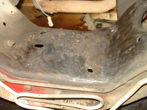 1993 Ford Bronco - The underside of a vehicle shows a heavily corroded frame and part of the exhaust system.