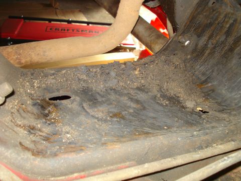 1993 Ford Bronco - The undercarriage of a red vehicle shows significant rust and dirt accumulation, with a Craftsman jack visible in the background.