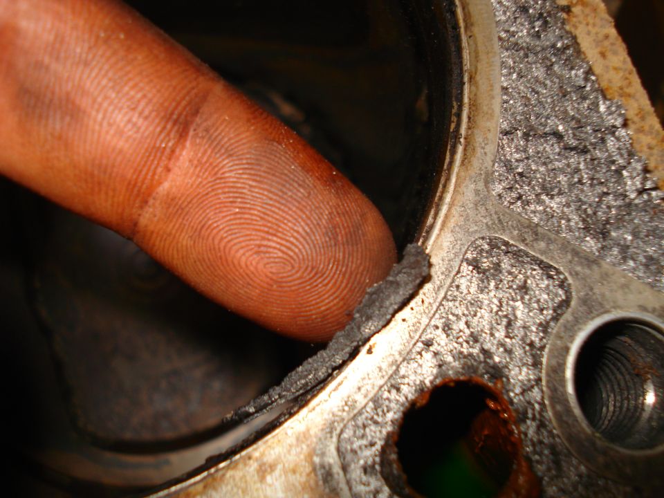 Finger pointing to damaged gasket on engine part