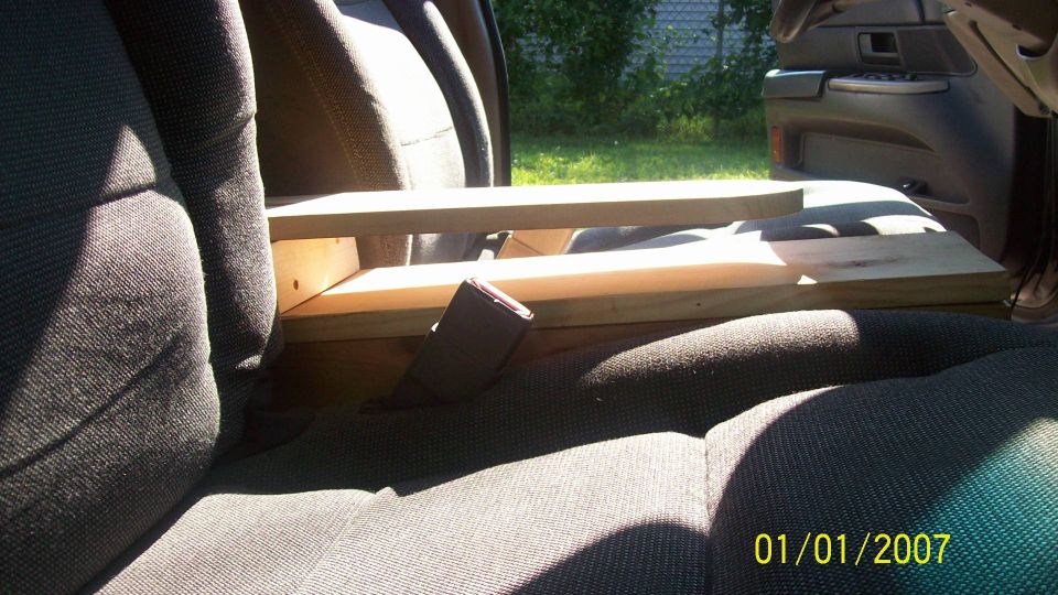 Car interior showing seats and a wooden structure between them. A seatbelt is visible