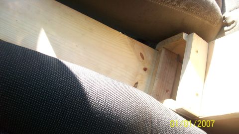 2004 Ford Crown Victoria - Wooden support structure installed beneath the seat of a vehicle, with visible fabric upholstery and sunlight.