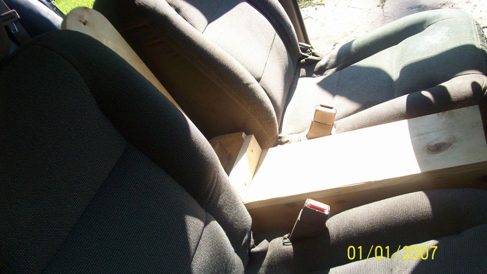 Car interior showing front seats with a wooden plank placed between them