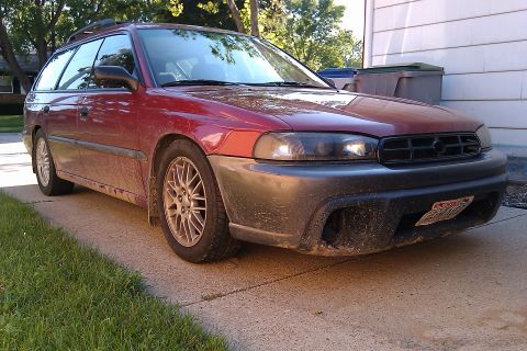 1998 Subaru Legacy - A dusty red 1998 Subaru Legacy station wagon is parked on a driveway, showing its front 3/4 view.