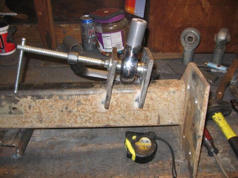 1989 Ford Bronco - A metal part, possibly a suspension component, is held by a clamp and features a threaded rod. A tape measure is visible nearby.