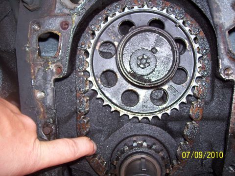 1978 Ford Bronco - Close-up view of an engine's timing chain and gears, with a hand indicating a specific point on the chain.