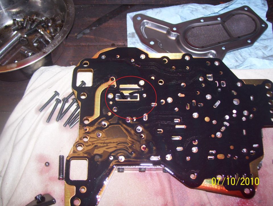Automatic transmission valve body with a red circle highlighting a component, parts and tools nearby
