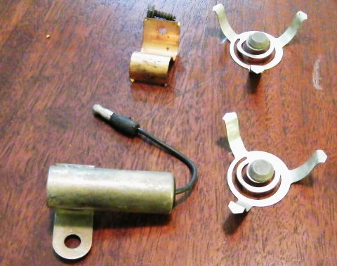 1968 Mercury Cougar - A close-up view of automotive ignition components, including a condenser and rotor clips, laid out on a wooden surface.