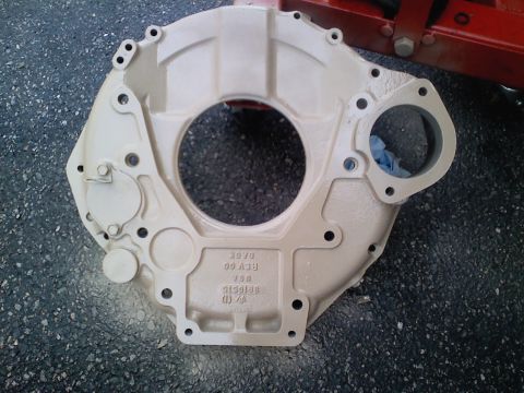 1990 Ford Bronco - A beige transmission bell housing sits on asphalt, showing casting marks and bolt holes.