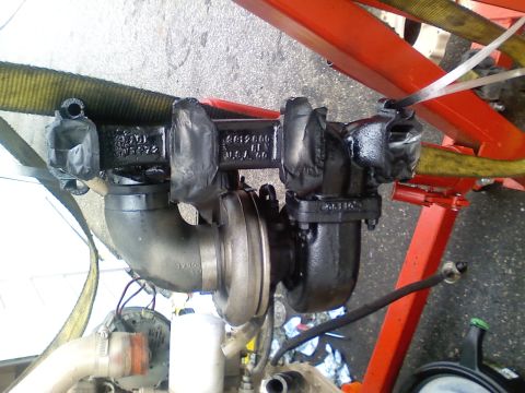 1990 Ford Bronco - Turbocharger assembly, likely for a diesel engine, being supported by a hoist.