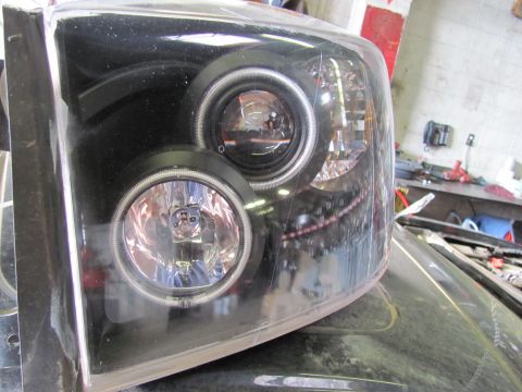 2005 Dodge 3500 - Close-up of a black headlight assembly a projector beam and a circular fog light.