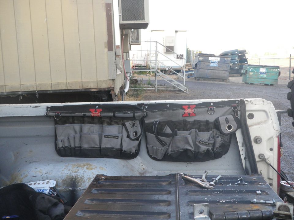 Pickup truck bed with two hanging tool organizers. A pair of vise grips rests on the tailgate