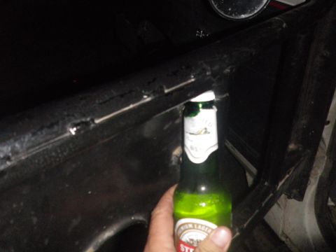 1991 Ford Bronco - A beer bottle is held up inside a vehicle, revealing a dark interior and a damaged metal bar.
