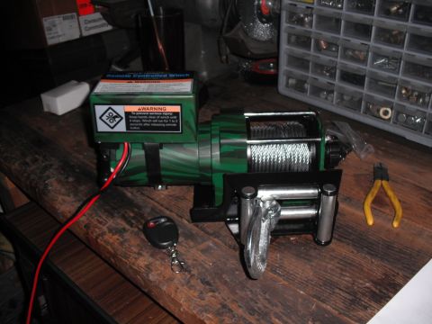 1991 Ford Bronco - A remote controlled winch is shown with its remote and a pair of pliers on a workbench.