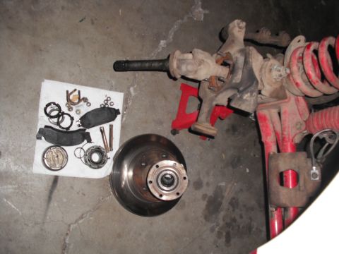 1991 Ford Bronco - Various parts of a vehicle's front axle and braking system are laid out on a concrete floor, suggesting a repair or upgrade in progress.