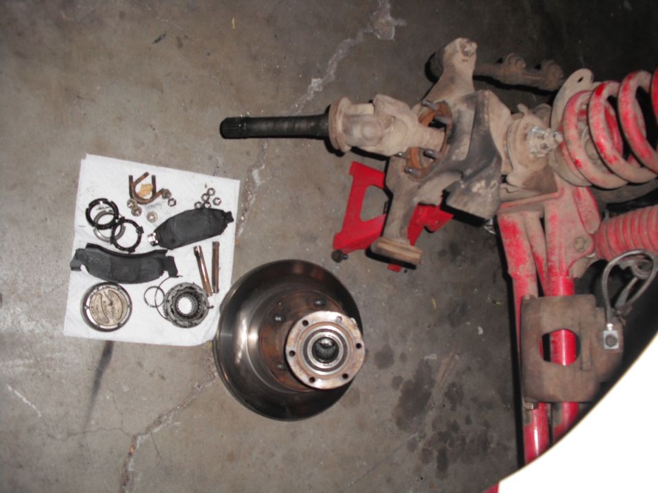 Disassembled front axle components and brake parts laid out on concrete floor