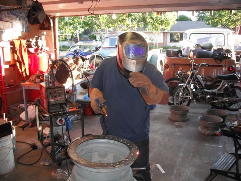 1991 Ford Bronco - Man welding a large metal ring in a garage with several vehicles in the background.