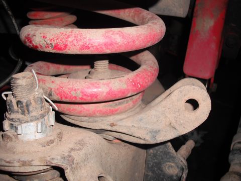 1991 Ford Bronco - This image shows a close-up view of dusty red suspension components, including a coil spring and control arm.
