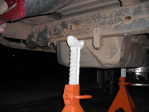 1991 Ford Bronco - The underside of a vehicle is supported by jack stands, revealing the frame, fuel tank, and suspension parts.