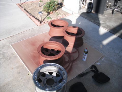 1991 Ford Bronco - Four beadlock wheels are laid out on a piece of plywood, with three of them coated in red oxide primer and one left bare.