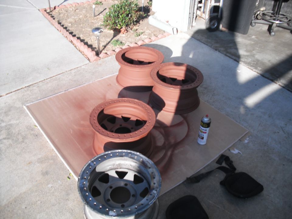 Four beadlock wheels, three painted red oxide, one bare metal, with spray can