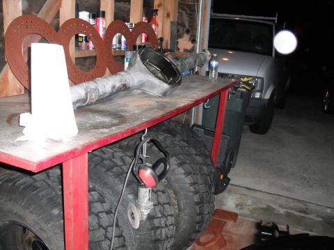 1991 Ford Bronco - A rear axle assembly rests on a workbench, with large tires and a grinder visible beneath.