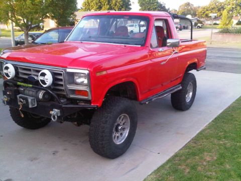 1986 Ford Bronco - This lifted red Ford Bronco has a custom front bumper with a winch and auxiliary lights.