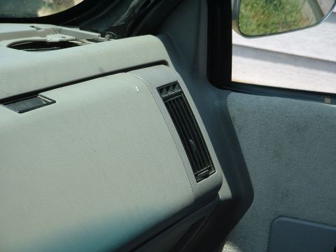 1994 GMC Suburban - Close-up view of the interior dashboard and door panel of a vehicle, with a side mirror reflecting the outside.