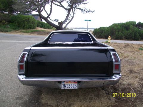 1973 Ford Ranchero - Rear view of a black Ford Ranchero parked on a roadside with a tree and bushes in the background.