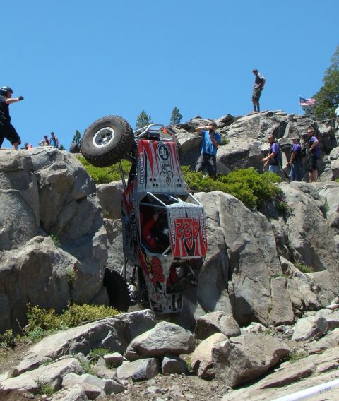 1970 Mercury Cougar - An off-road buggy is precariously balanced on its side amidst a rocky terrain, with spectators observing the background.