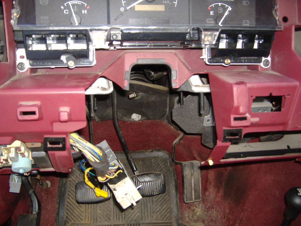 Dashboard wiring and pedals in a truck, looks like the steering column area is exposed