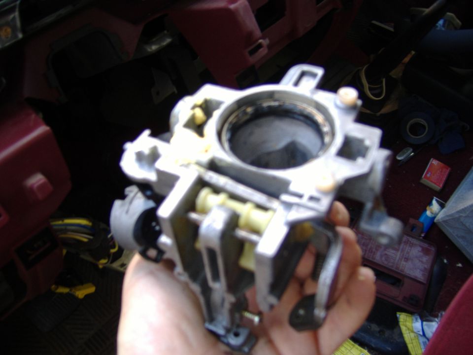 Hand holding a disassembled steering column ignition switch housing with yellow plastic components