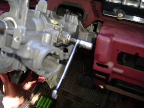 1995 Ford F-150 - Close-up of a vehicle's steering column assembly, showing the ignition cylinder housing and a tool.